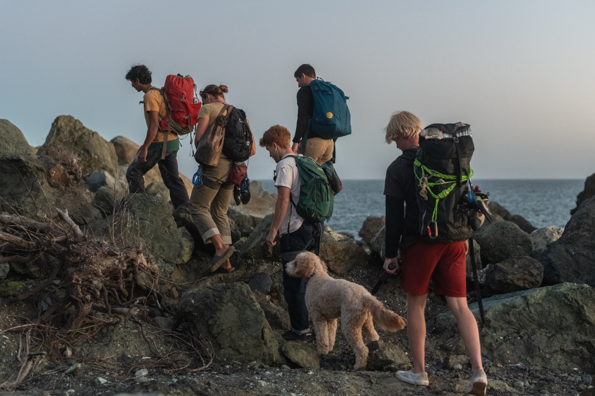 A crew of climbers with packs and their dog heading out along the rocks at dusk